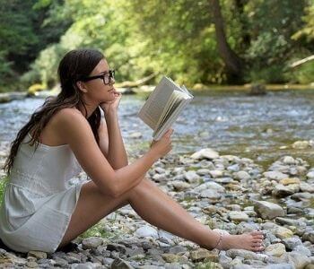 河原で読書する眼鏡の女性