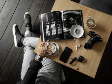 テーブルの上にカメラ、雑誌を置いてコーヒーを飲む男性