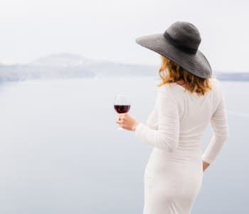 帽子を被り、ワインを飲みながら湖を見るセレブな女子