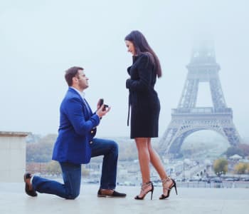 男性がエッフェル塔の前で膝をつき女性にプロポーズしている