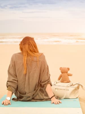 海辺で一人でぬいぐるみと一緒に座っている女性